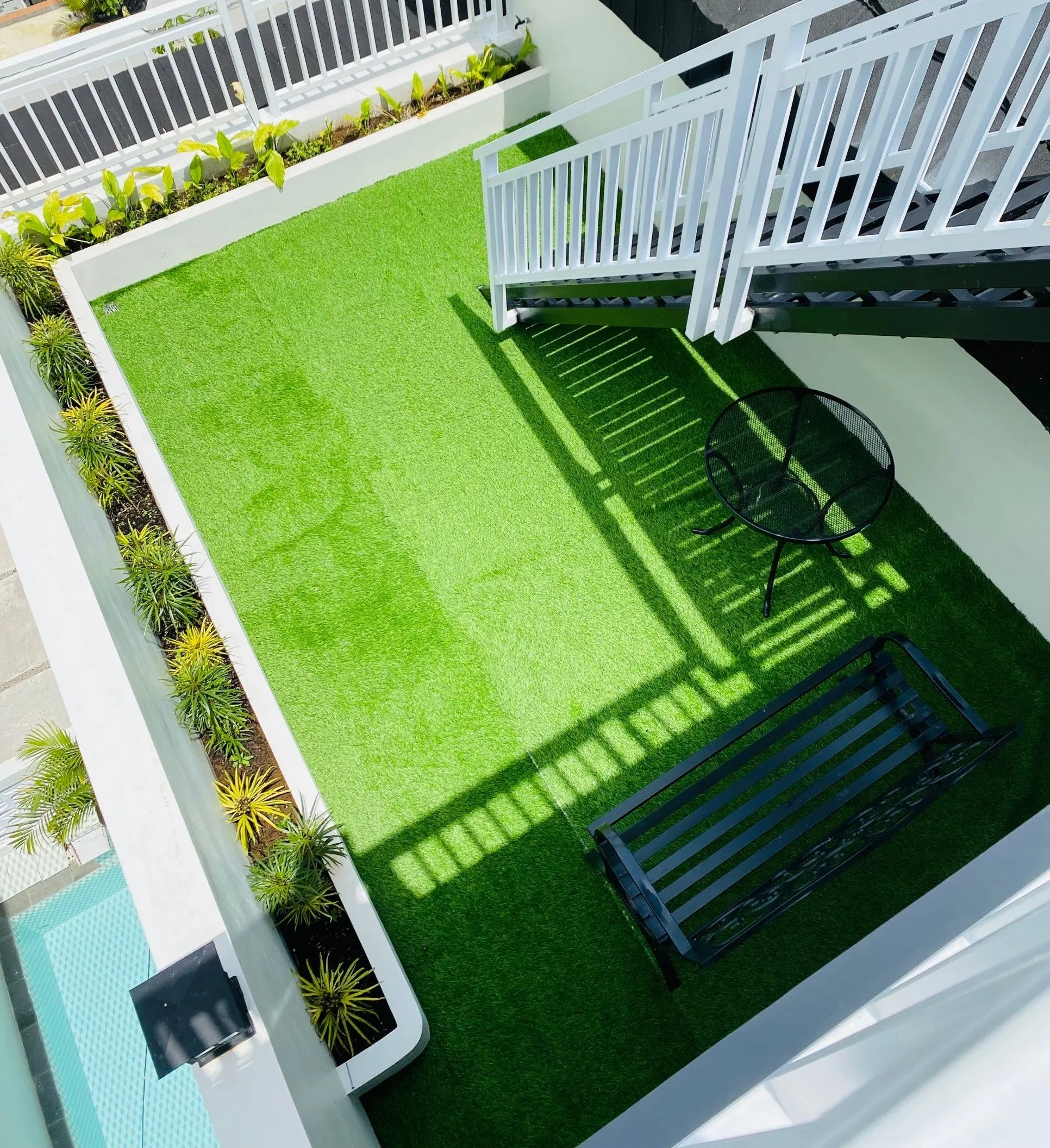 Artificial turf laid on a small rooftop patio with a bench and chair